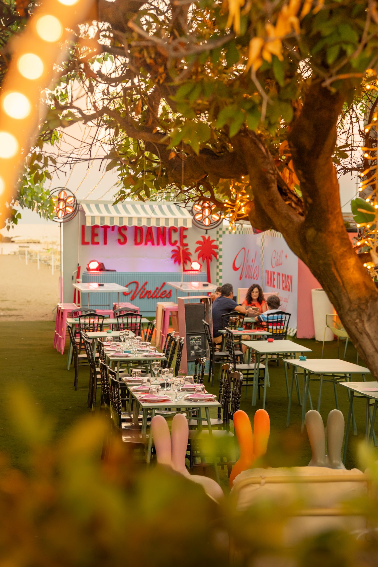 Il giardino di Viniles al tramonto, tavoli sotto l'albero e luci accese